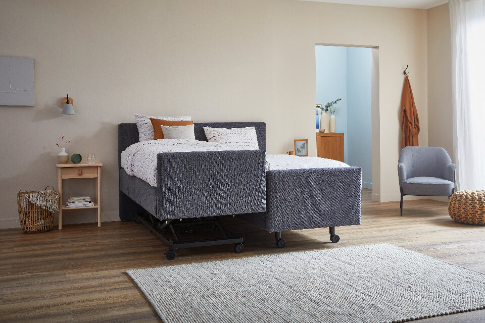 Grijs boxspring bed op wielen wat aan een kant hoog laag kan en aan een kant verstelbaar is
